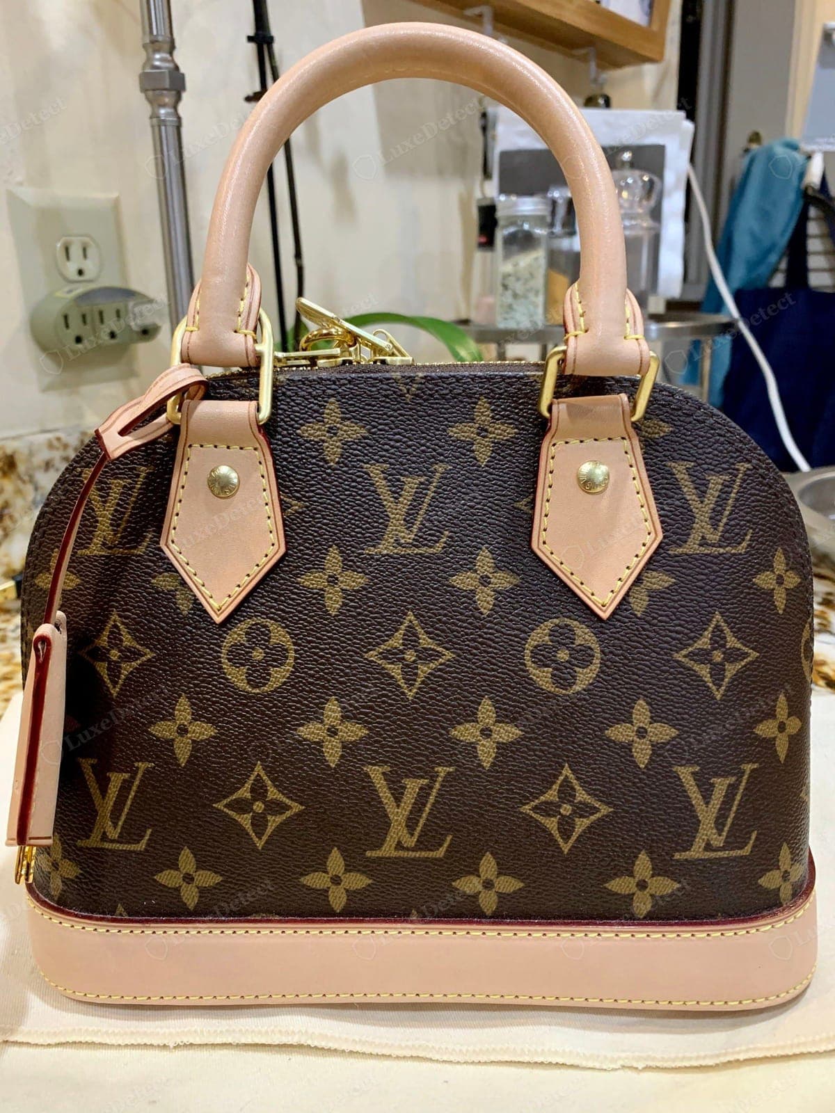 Counterfeit LV Alma — the Monogram sits slightly large and reads too bold and dark with a faint plastic sheen, and the vachetta is a flat uniform pinkish-tan with none of the natural tonal variation of genuine raw leather