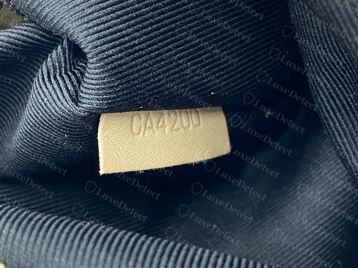 Lengüeta del código de fecha de una Bumbag original: una pequeña lengüeta de piel crema estampada con CA4200, junto a la cremallera de latón sobre un forro oscuro