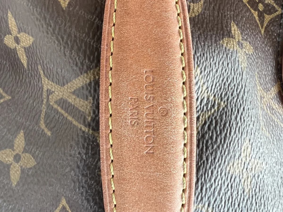 Poignée supérieure d'un Bumbag authentique en gros plan : LOUIS VUITTON PARIS estampillé sur la longueur de la vachetta, avec une marque déposée au-dessus, et des coutures jaunes régulières des deux côtés