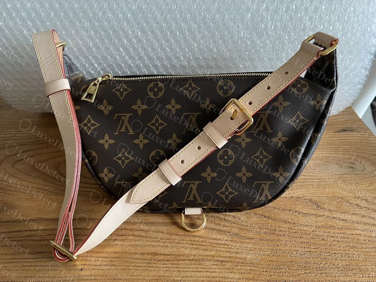 Bumbag Monogram authentique avec sa sangle réglable en vachetta et ses boucles en laiton, photographié à plat sur une surface en bois
