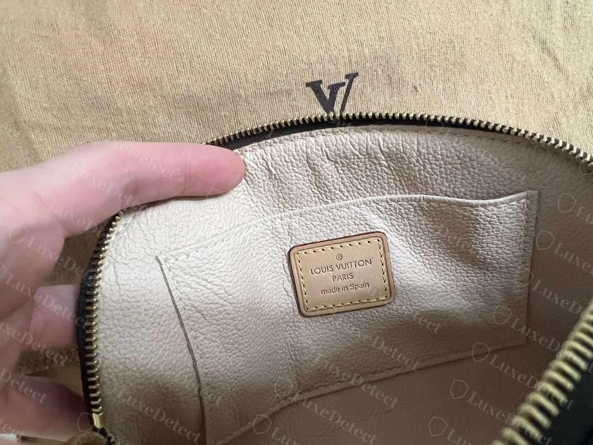 Intérieur d'une Cosmetic Pouch authentique : une petite languette en cuir estampillée LOUIS VUITTON PARIS made in Spain, cousue en jaune sur une doublure crème à l'intérieur d'une poche plate