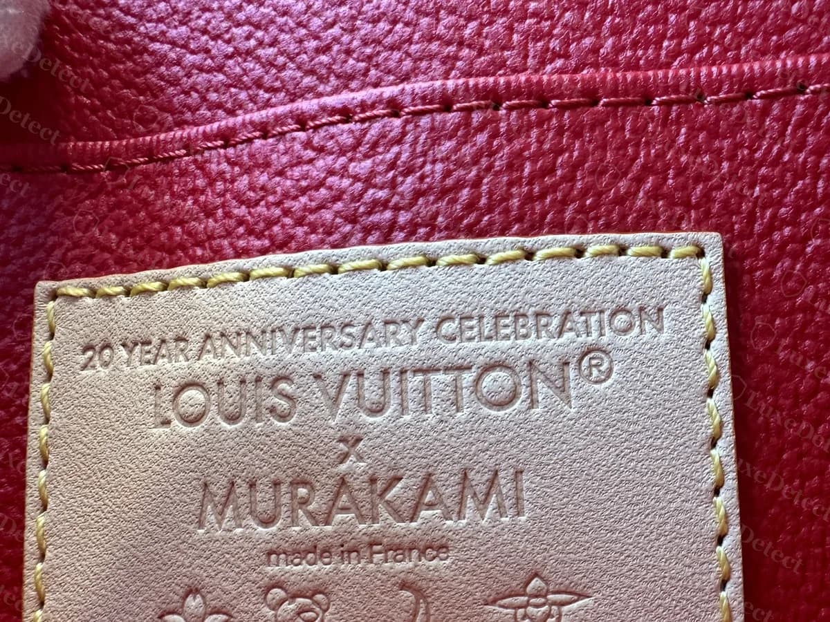 Innenlasche einer echten Louis Vuitton x Murakami Cosmetic Pouch: 20 YEAR ANNIVERSARY CELEBRATION, LOUIS VUITTON, MURAKAMI und made in France, mit kleinen Motiven darunter, auf rotem Futter