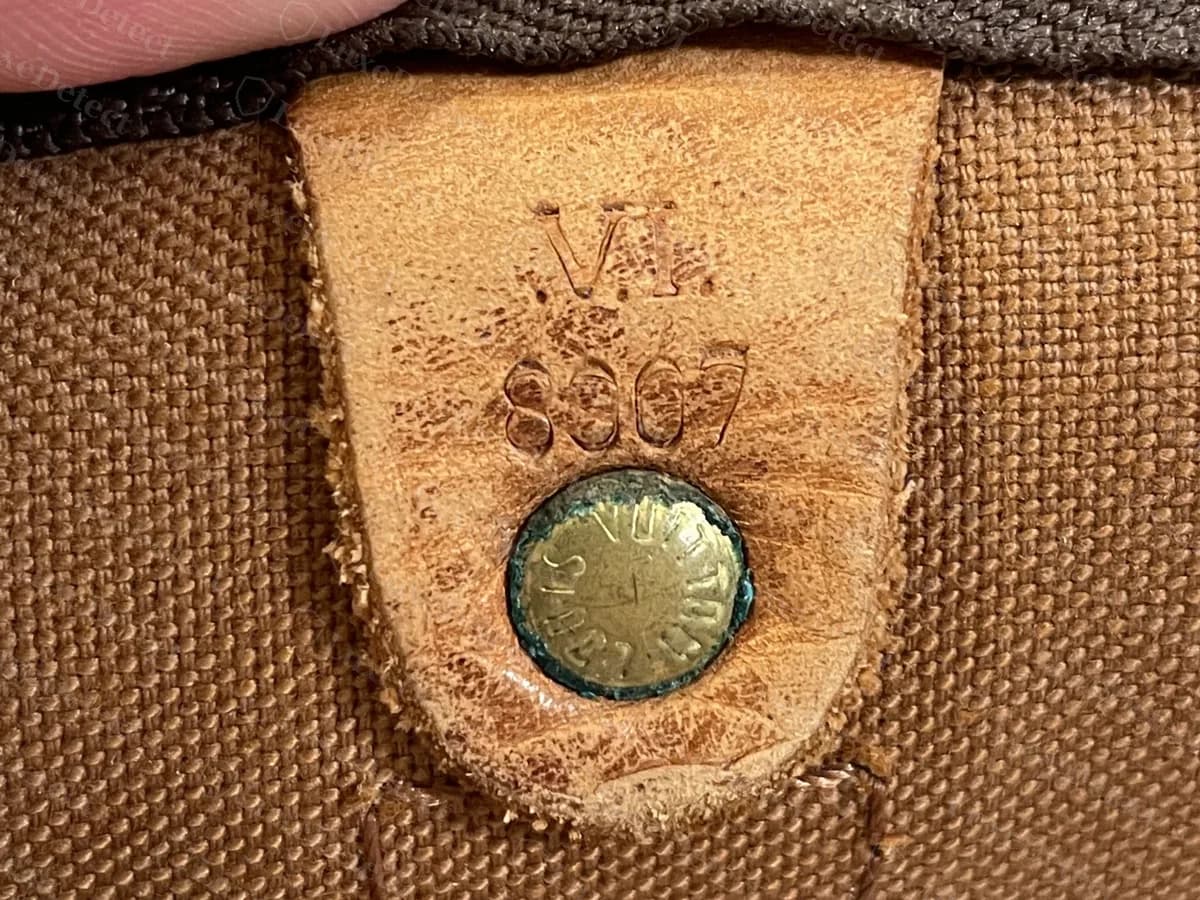 Una targhetta Louis Vuitton molto consumata su un Keepall Bandoulière: le lettere VI sono leggibili, ma le quattro cifre sotto si sono consumate nella pelle e sono ambigue