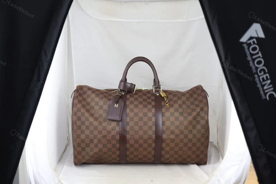 Authentic Damier Ebène Keepall showing the checkerboard grid held sharp and consistent across the full panel, including around the handle straps