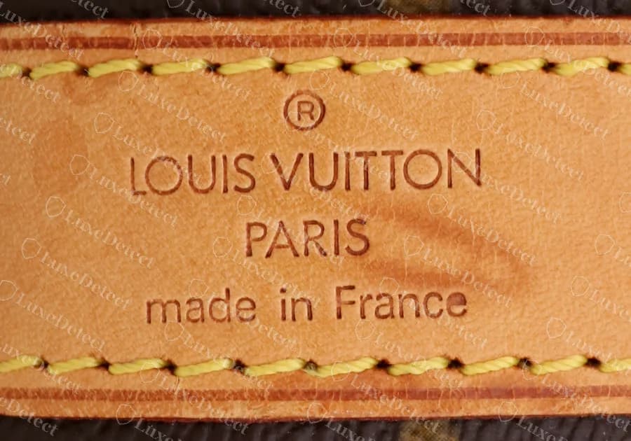El sello grabado en caliente exterior de una banda de vachetta de un Keepall Bandoulière 45 original: ® encima de LOUIS VUITTON, luego PARIS y made in France, presionado de forma pareja