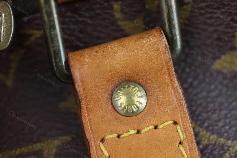 Authentic vachetta pull-tab rivet on a Keepall handle base — crisply struck lettering at consistent depth