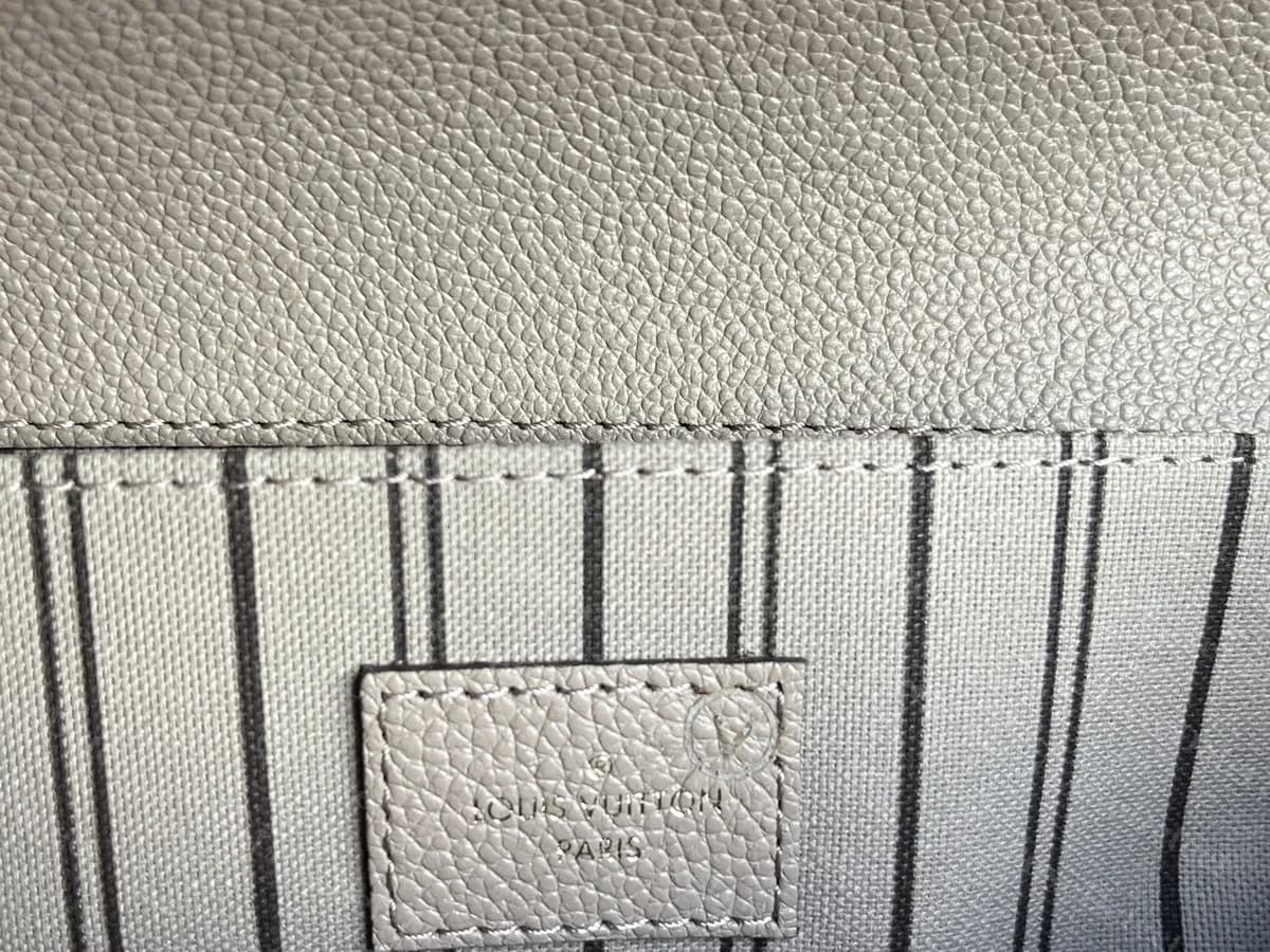 Genuine grey Empreinte Metis interior tab from a bag with a chip: a blind-stamped tab on the striped lining, the lettering faint and tone on tone