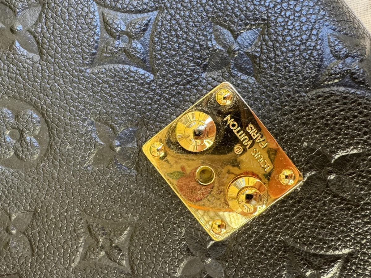 Genuine Empreinte Metis lock plate shown turned sideways: "LOUIS VUITTON PARIS" stamped along the plate, two domed studs and four small corner screws