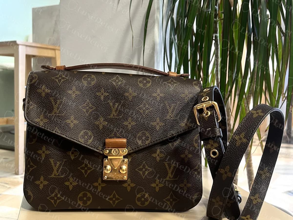 Genuine Monogram canvas Pochette Metis on a table with its detachable strap: a top handle, a flap with the S-lock, and the strap running off to the right