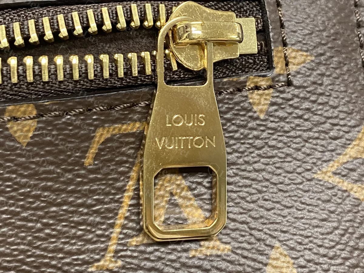 Genuine zip pull on the back pocket of a Monogram Metis: a flat gold-tone pull stamped LOUIS VUITTON in two lines, with an open slot at the bottom