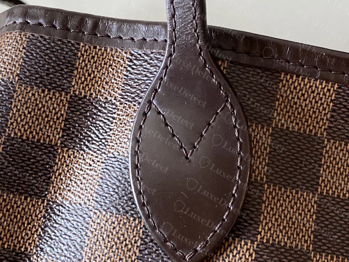 Echtes Henkelende einer Damier-Ebène-Neverfull: dunkles Leder, spitz zugeschnitten mit einem aufgenähten V, auf kariertem Canvas