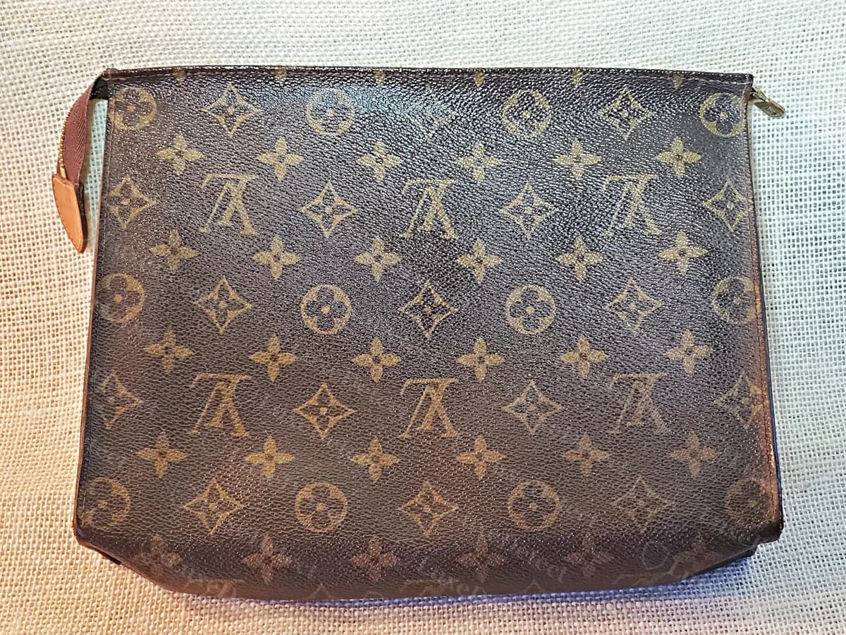 Toiletry Pouch 26 ancienne et authentique, classée comme antérieure aux codes date : une pochette Monogram plate avec une languette en vachetta naturelle à l'extrémité de la fermeture éclair