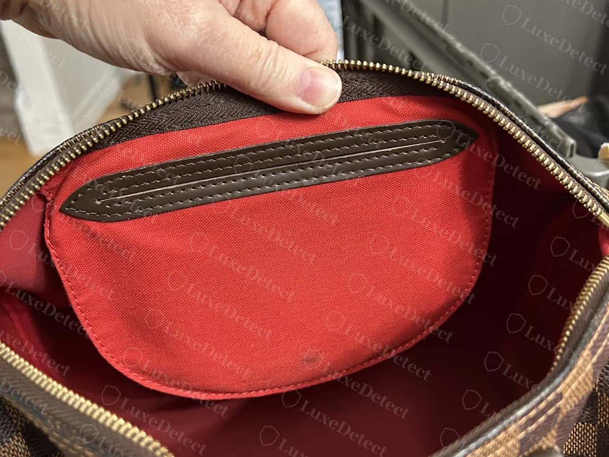 Interior de un Speedy Damier Ebène original: un forro de lona roja con un bolsillo plano ribeteado en piel oscura