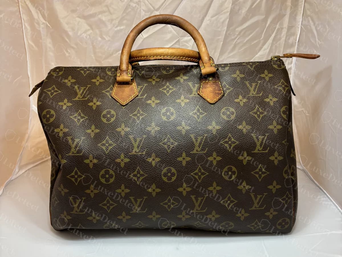 Genuine Monogram Speedy 30 from the front: a rounded, drum-shaped body, two vachetta handles and a stitched zip, photographed on a plain backdrop