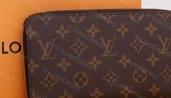 Genuine LV monogram canvas — warm chocolate brown with a red undertone, camel motifs at consistent scale, cut deliberately at the zip seam