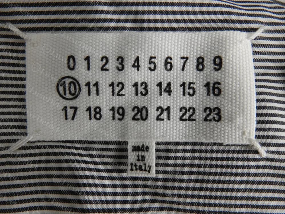 Genuine Maison Margiela numbered clothing label: a white woven label with the numbers 0 to 23 in three rows and one number circled, held at the four corners by small white stitches, with a small made in Italy label beneath