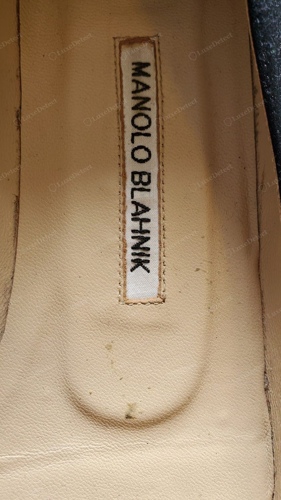 Semelle intérieure contrefaite Manolo Blahnik — une étiquette « MANOLO BLAHNIK » crasseuse aux lettres irrégulières et déformées, avec des coutures tremblantes autour d'un bord qui s'effiloche