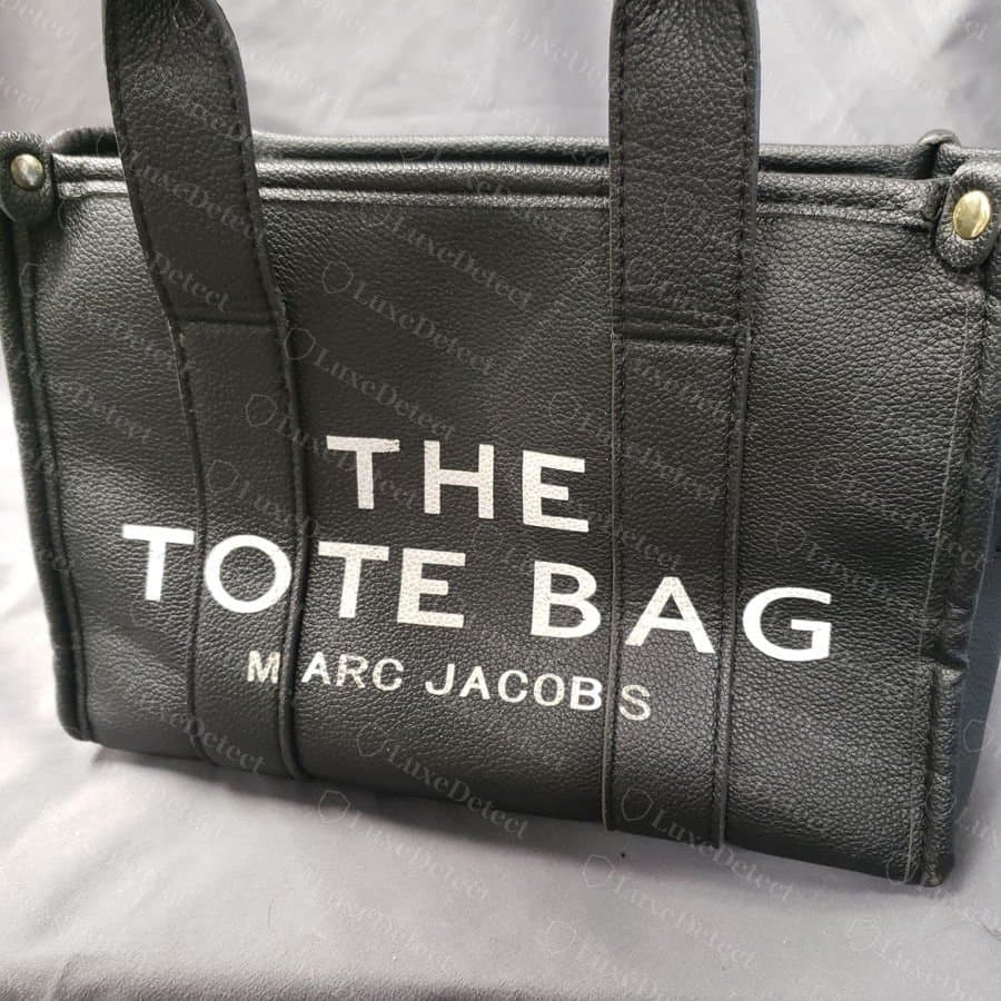 Logo avant d'un faux Marc Jacobs The Tote Bag : lettrage plus lourd avec un espacement irrégulier dans « MARC JACOBS »