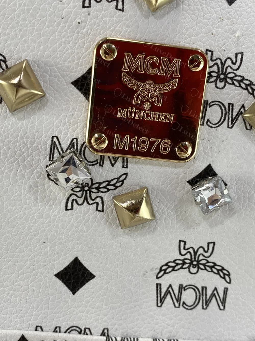 Placa MCM Stark falsa con un tinte rojo y cristales sueltos entre los tachones en un bolso Visetos blanco