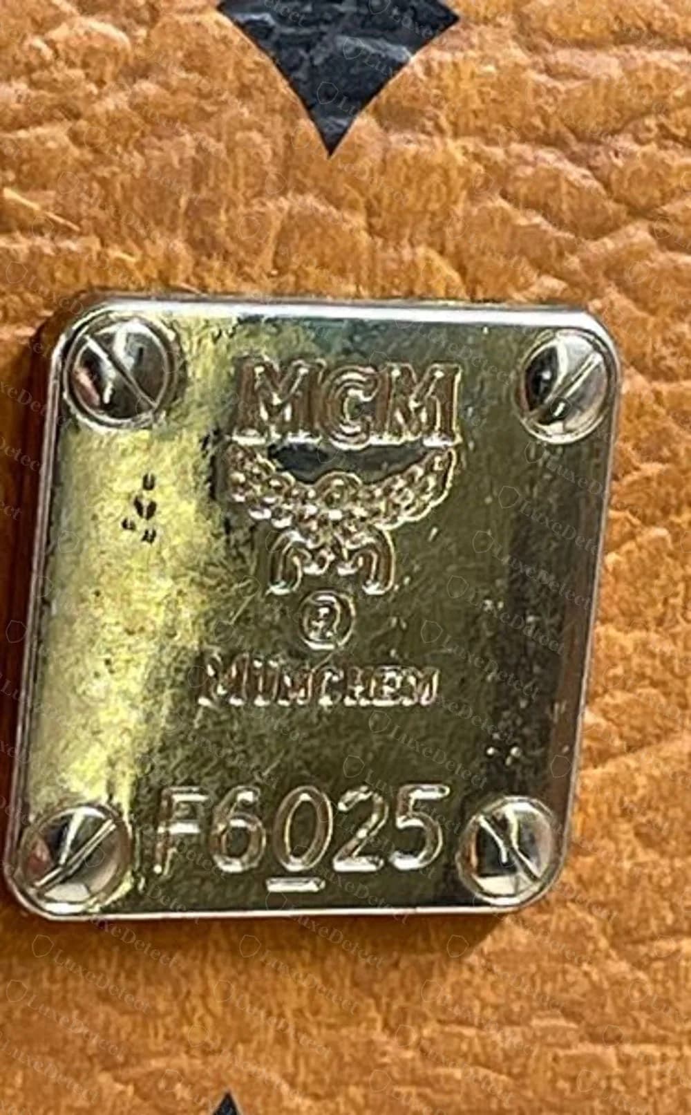 Counterfeit MCM plate on cognac Visetos with smeared MÜNCHEN lettering and a filled-in crest above the serial F6025