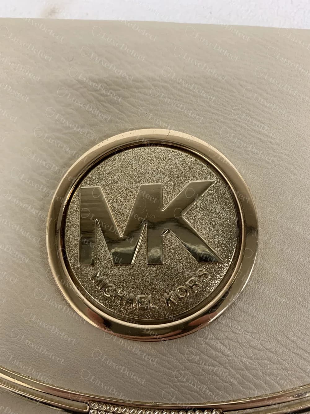 Fälschung: MK und MICHAEL KORS erhaben auf einer massiven sandgestrahlten Metallscheibe an einer cremefarbenen Klappe