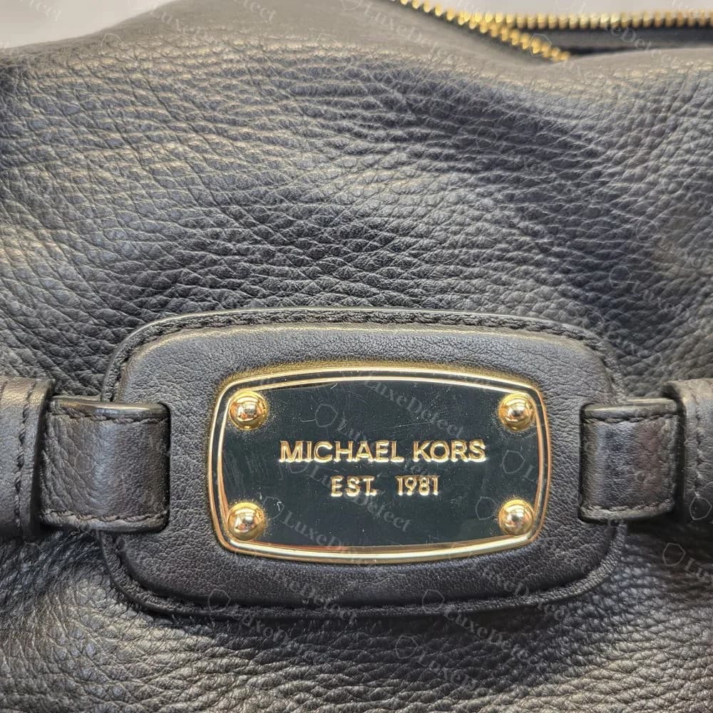 Echte Plakette MICHAEL KORS EST. 1981 auf schwarzem genarbtem Leder: ein echtes Zeichen, das Fälschungen kopieren, also für sich kein Warnsignal