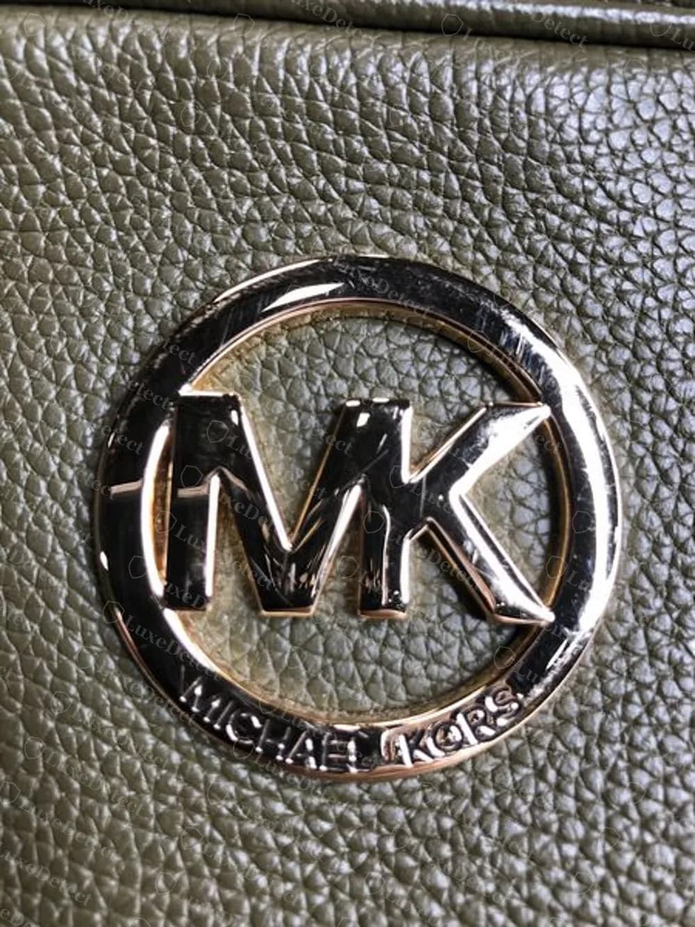 Medallón Fulton original sobre piel granulada verde oliva: el grano de la piel del propio bolso se ve a través del anillo abierto, con la MK sostenida por el anillo y MICHAEL KORS a lo largo del anillo