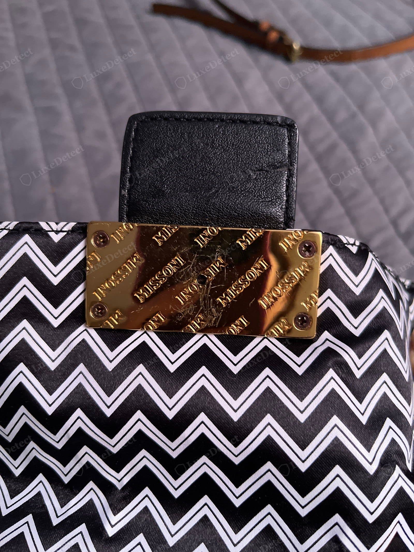 Counterfeit Missoni — the zigzag is flat-printed on a cheap satin nylon with hard white outlines (no knit texture, blank reverse), finished with a scratched gold "MISSONI"-repeat logo plate screwed to the panel