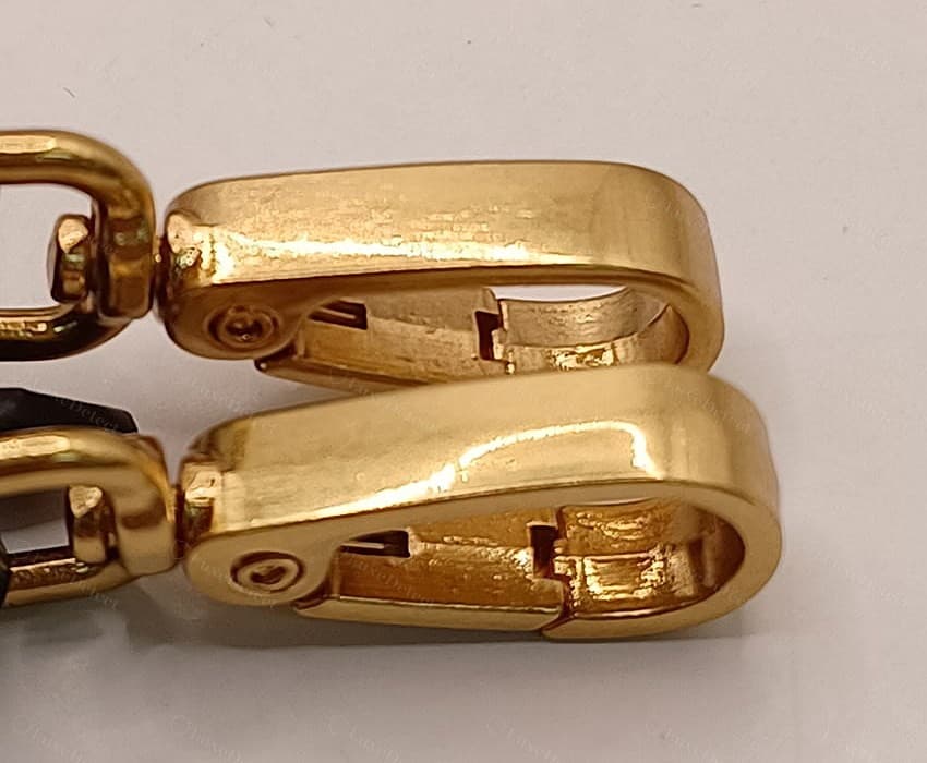 Gefälschte Miu-Miu-Beschläge: hellgoldene Riemenkarabiner mit sichtbarer Gussnaht am Rücken, Werkzeug- und Feilspuren und rauen, unbearbeiteten Innenflächen