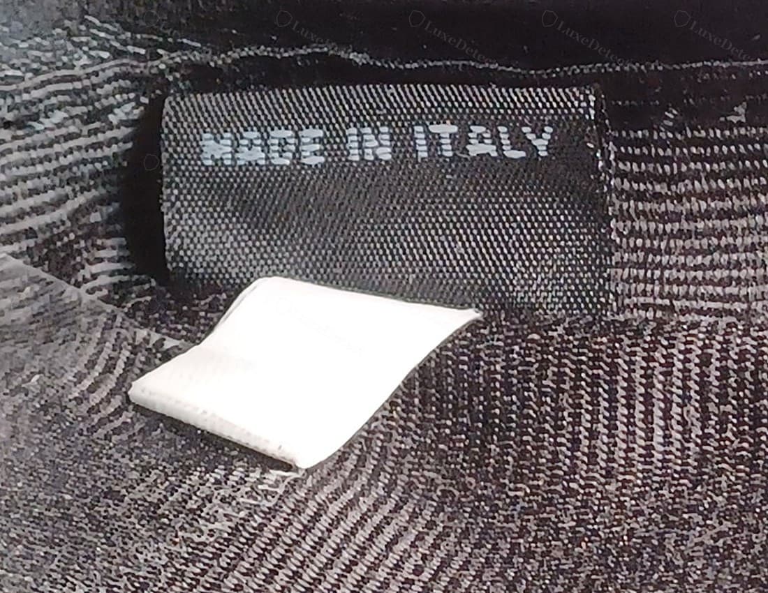 Gefälschtes Miu-Miu-Innenfutter: gar keine Metallplatte, sondern nur ein direkt ins Futter gewebtes „MADE IN ITALY“ in dünner, pixeliger Webart mit gebrochenen, ungleichmäßigen Buchstaben, daneben ein schlichtes weißes Fabriketikett