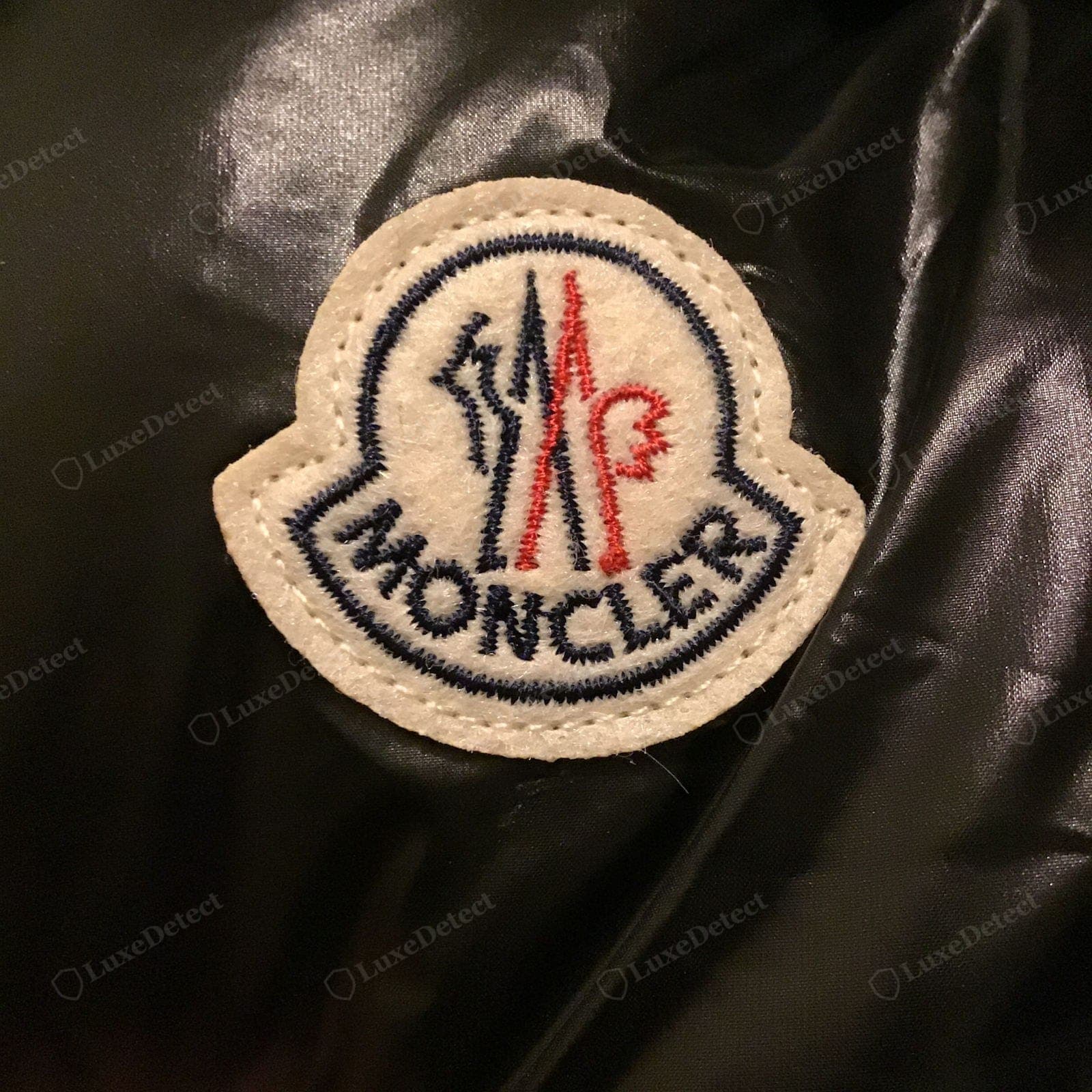 Gefälschtes Moncler-Ärmelabzeichen — unscharfes oder falsch proportioniertes Logo, lose oder ungleichmäßige Nähte, falsche Filzfarbe