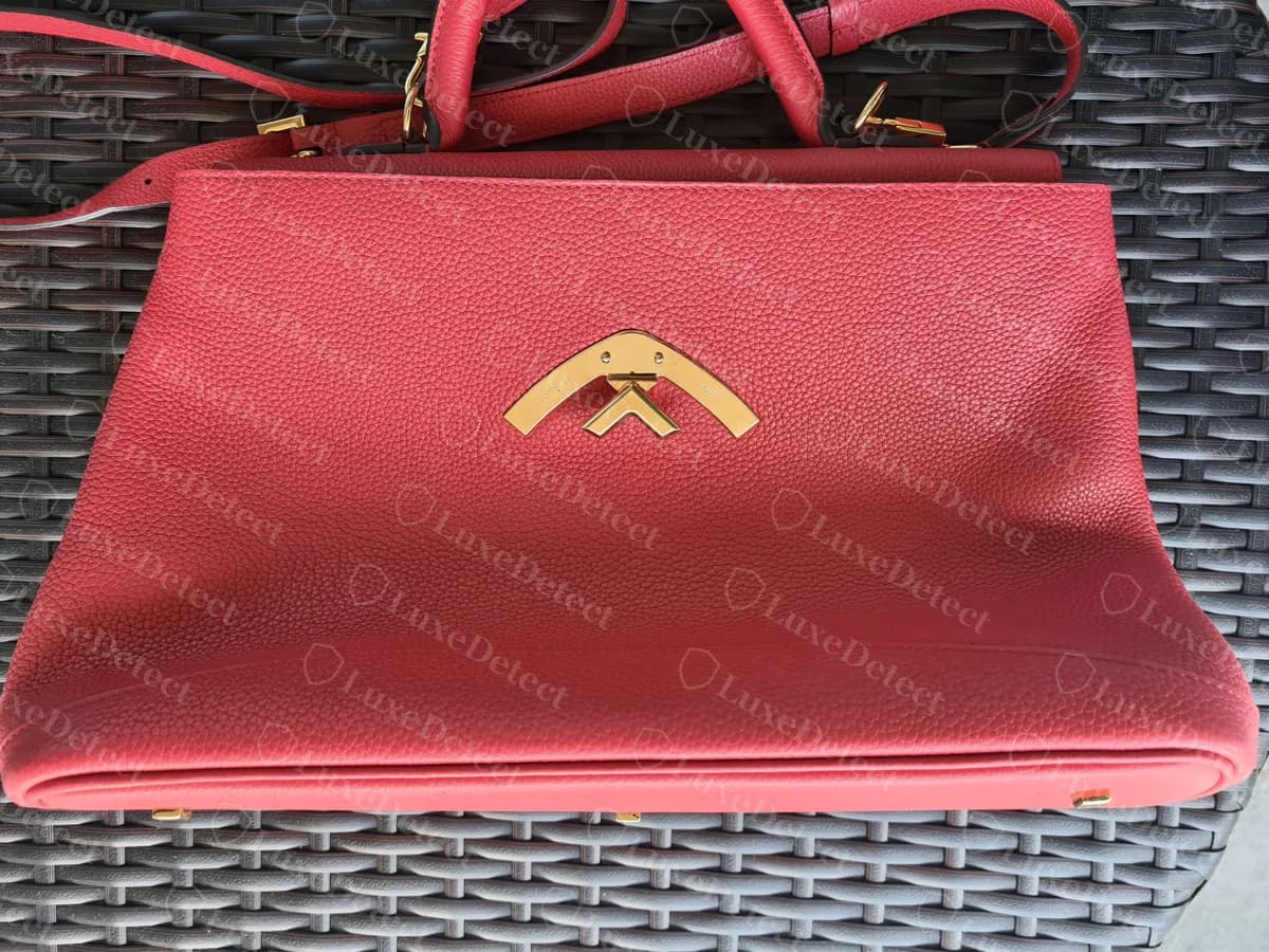Counterfeit red Moynat Gabrielle with a gold-tone chevron clasp, photographed with its shoulder strap