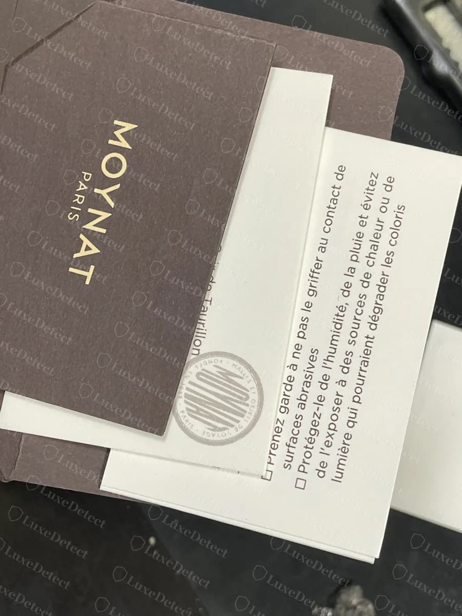 Genuine Moynat card envelope with the condensed MOYNAT logo in gold, alongside the care booklet
