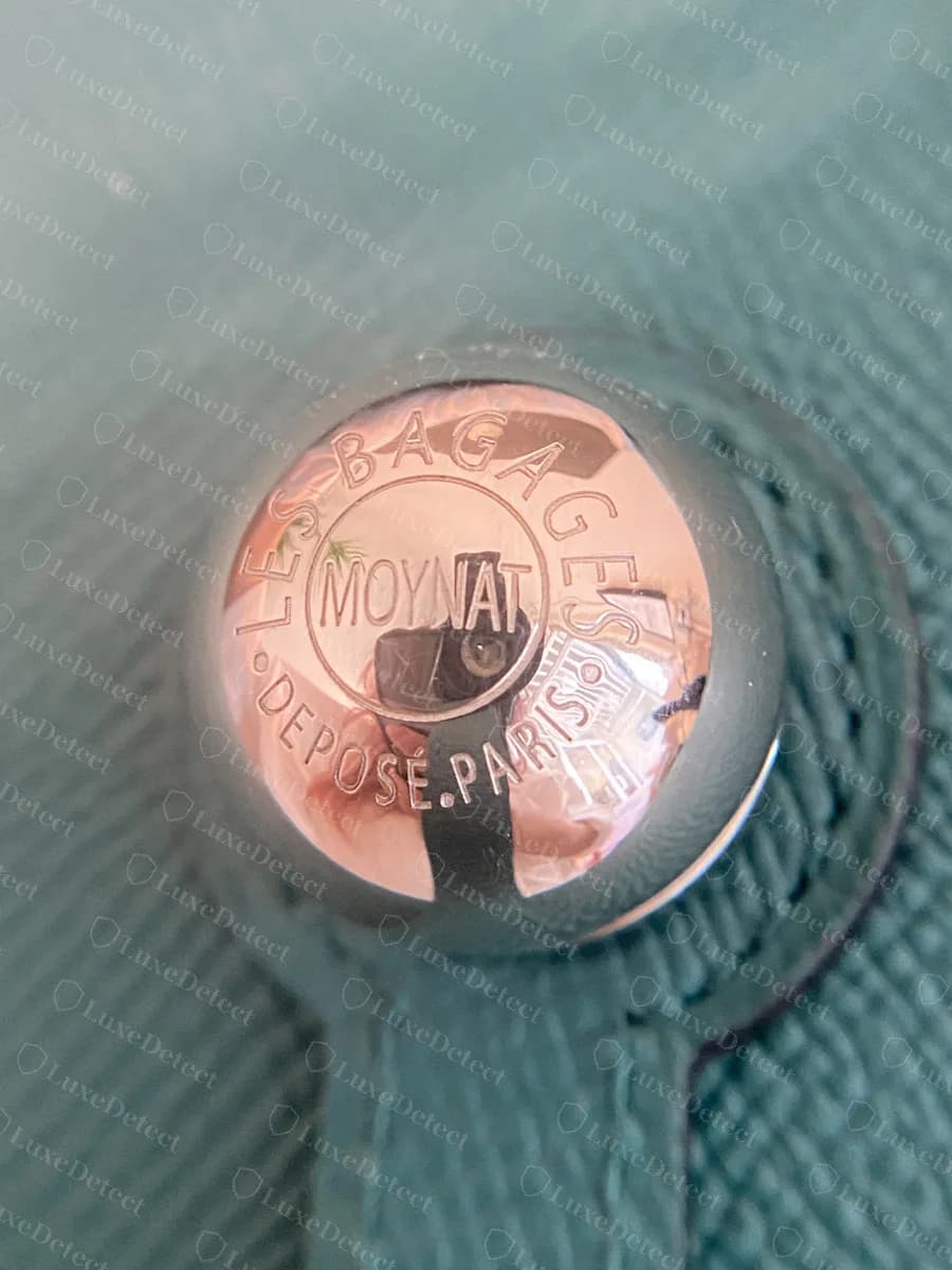 Genuine Moynat domed metal button engraved LES BAGAGES MOYNAT DÉPOSÉ PARIS on a teal leather flap bag