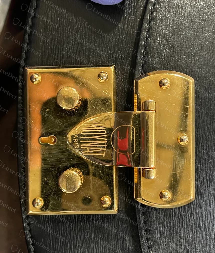 Counterfeit Moynat Flori gold-tone trunk lock with the condensed MOYNAT logo on its tongue