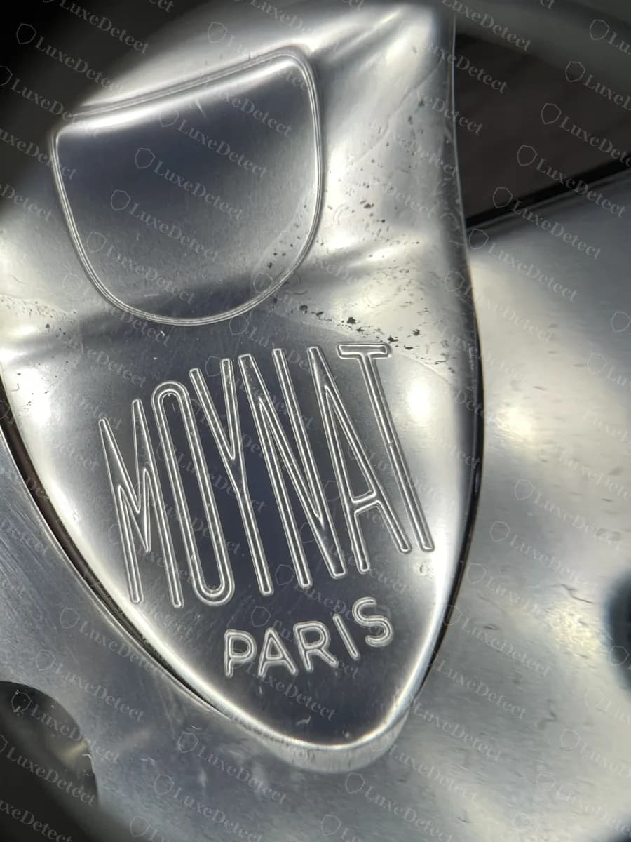 Genuine Moynat Flori lock tongue engraved with the condensed MOYNAT logo over PARIS, under magnification