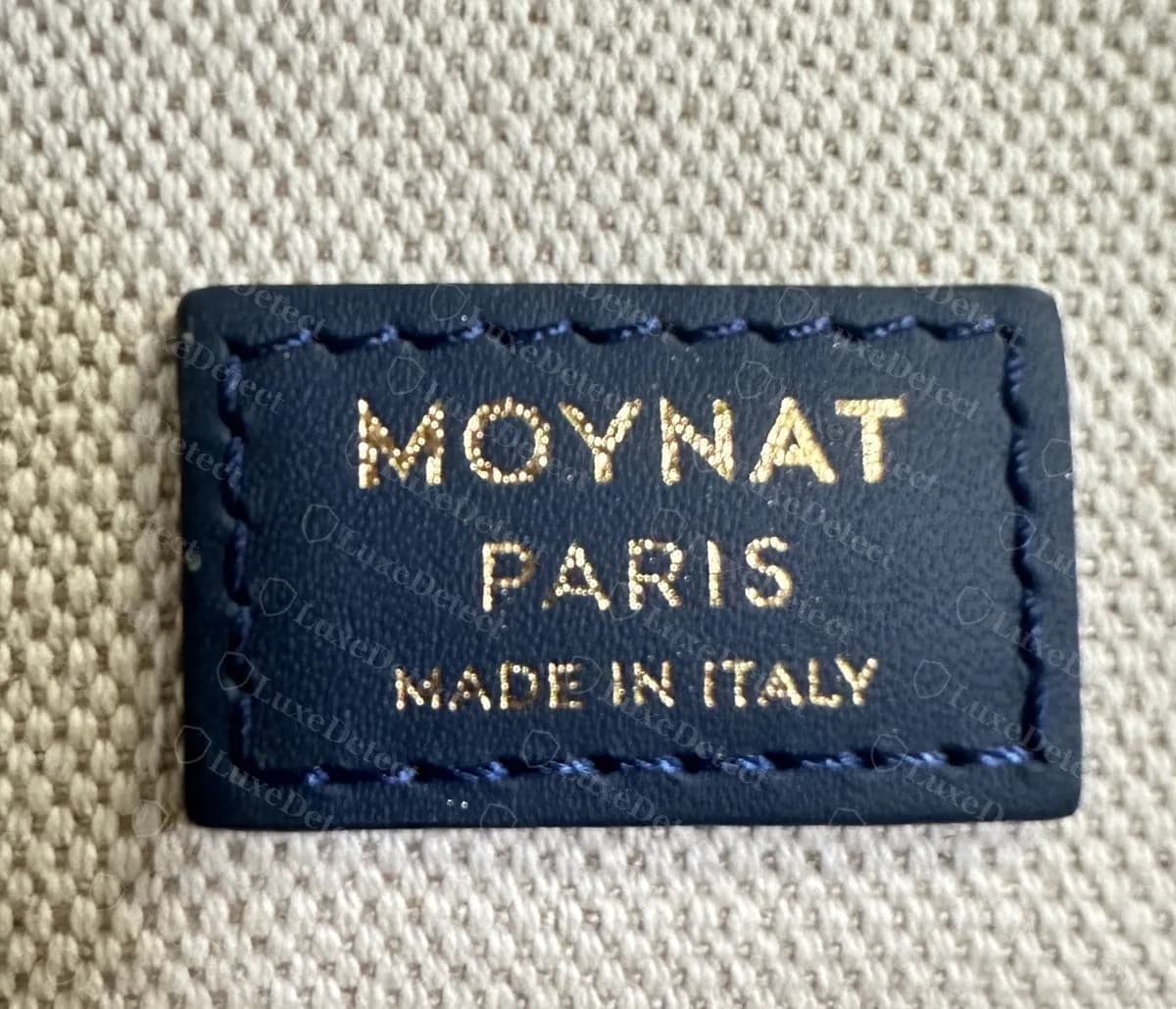 Counterfeit Moynat Oh! Tote label reading MOYNAT PARIS MADE IN ITALY with heavy foil lettering and loose wavy edge stitching