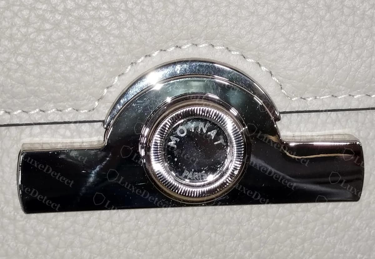 Cierre giratorio de un Moynat Réjane falsificado, cara lisa grabada con MOYNAT y PARIS y un borde acanalado, muy parecido al cierre genuino de tamaño pequeño