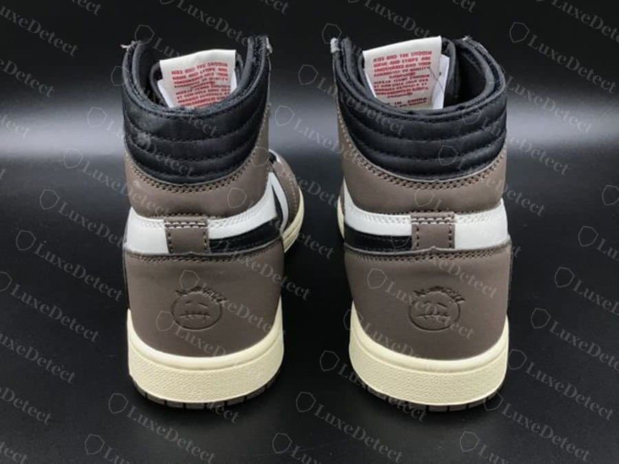 Gefälschter Travis Scott x Air Jordan 1 High „Mocha“, Rückansicht: die Fersenlasche und das geprägte Smiley auf einer glatten, gleichförmig wirkenden Fersenkappe