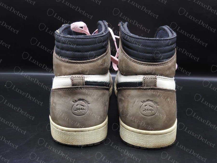 Travis Scott x Air Jordan 1 High “Mocha” originale, vista posteriore: la linguetta del tallone e lo smiley Cactus Jack in rilievo sul contrafforte, su nubuck con pelo texturizzato