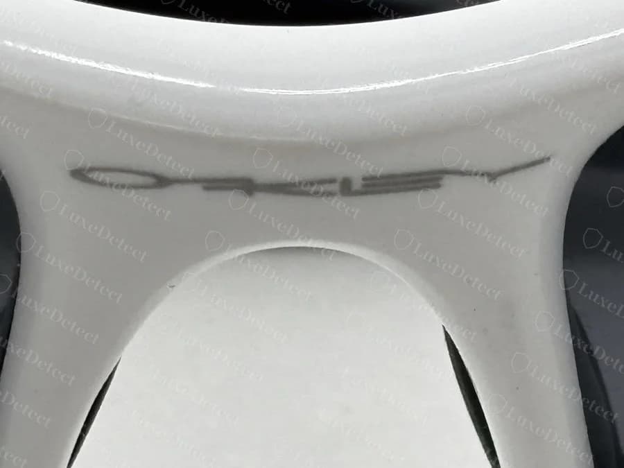 Counterfeit Oakley Flak bridge etch — the OAKLEY wordmark crooked, with letters sitting at inconsistent heights and uneven spacing