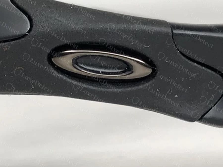 Close macro of an Oakley Flak O icon and hinge from a counterfeit-outcome listing, shown at comparable detail for reference