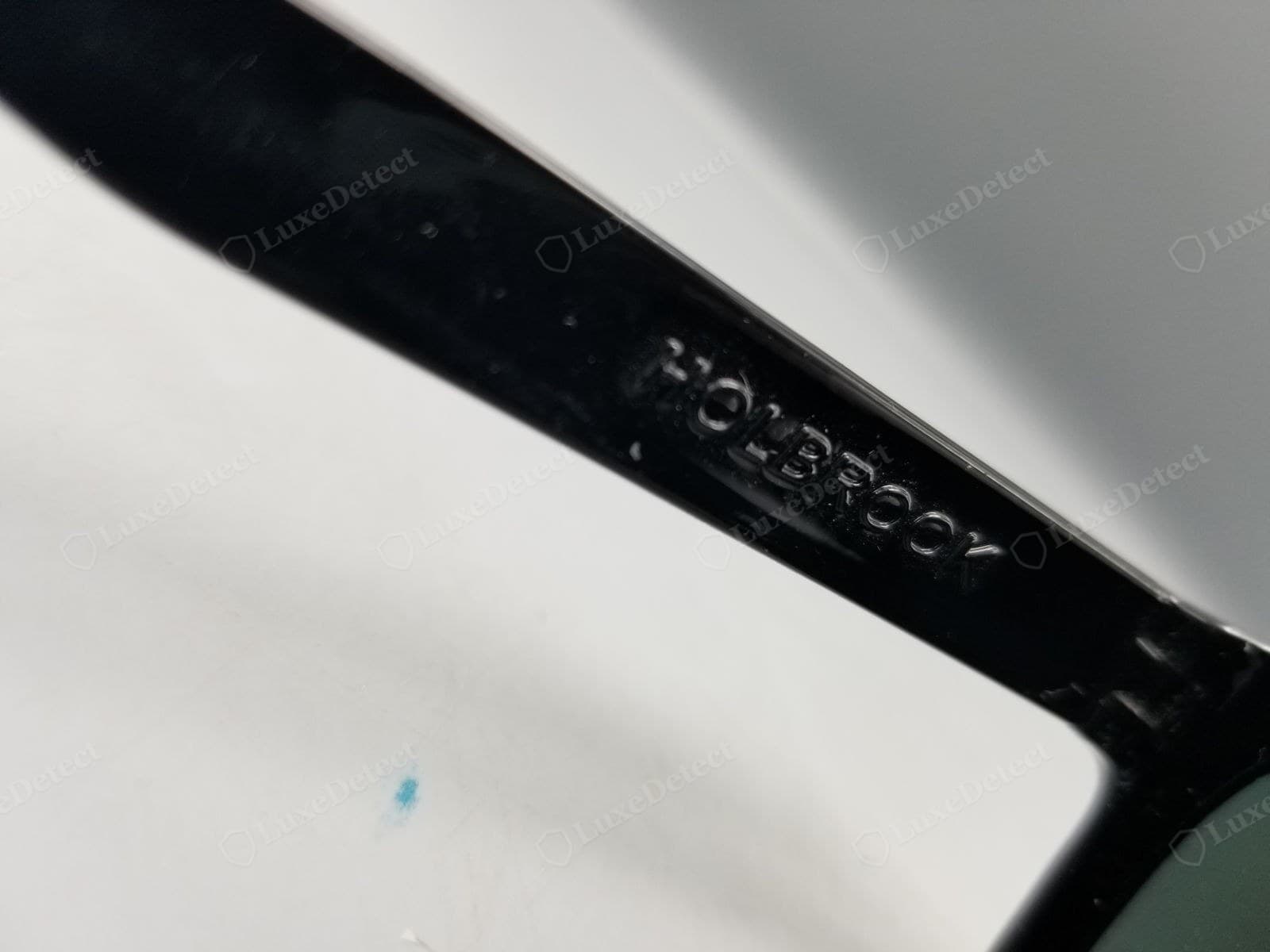 Gefälschter Oakley-Holbrook-Bügel: der erhabene Name HOLBROOK mit ausgefransten, ungleichmäßigen Buchstaben geformt; auf diesem Foto ist keine Codezeile zu sehen