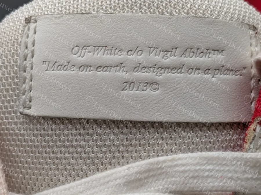 Etiqueta de la lengüeta en relieve en el interior de una zapatilla Off-White genuina que dice "Off-White c/o Virgil Abloh™ Made on earth, designed on a plane 2013"; las falsificaciones copian esta etiqueta