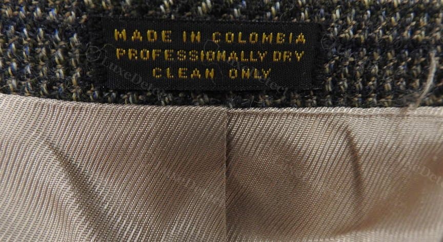 Authentic care tag — "Made in Colombia / Professionally Dry Clean Only" in gold thread on a black woven strip, sewn beside the wool blazer's interior seam