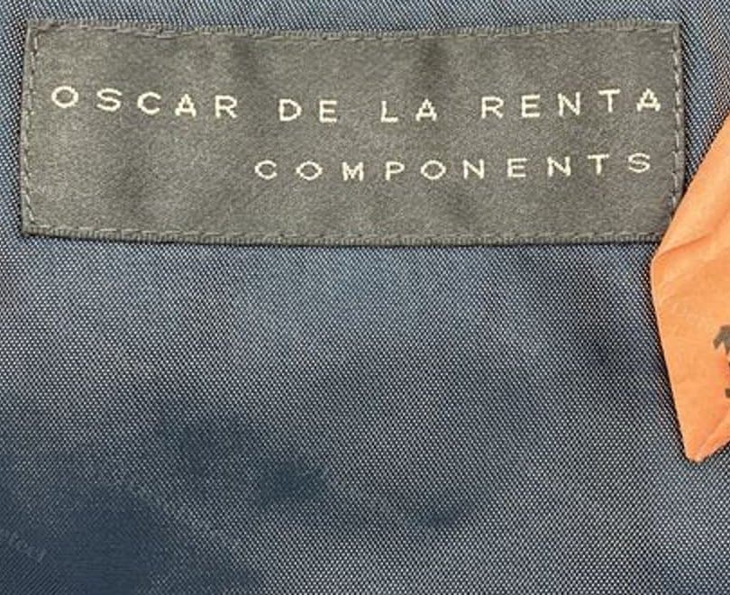 Counterfeit garment's interior label — plain block sans-serif reading "Oscar de la Renta Components" on a dark ground, no cursive signature