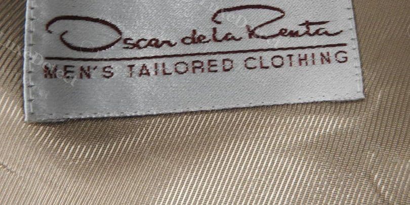 Authentic Oscar de la Renta interior label — cursive signature script above "MEN'S TAILORED CLOTHING" in serif block letters, clean satin ground