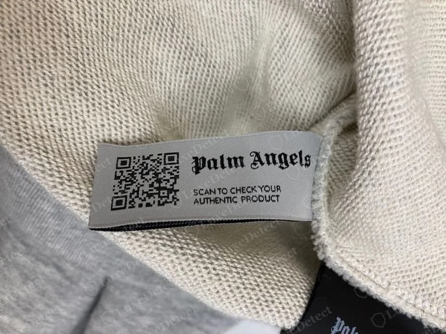 Genuine Palm Angels grey woven label with a QR code, the name in gothic lettering and the words SCAN TO CHECK YOUR AUTHENTIC PRODUCT, sewn inside a grey hoodie