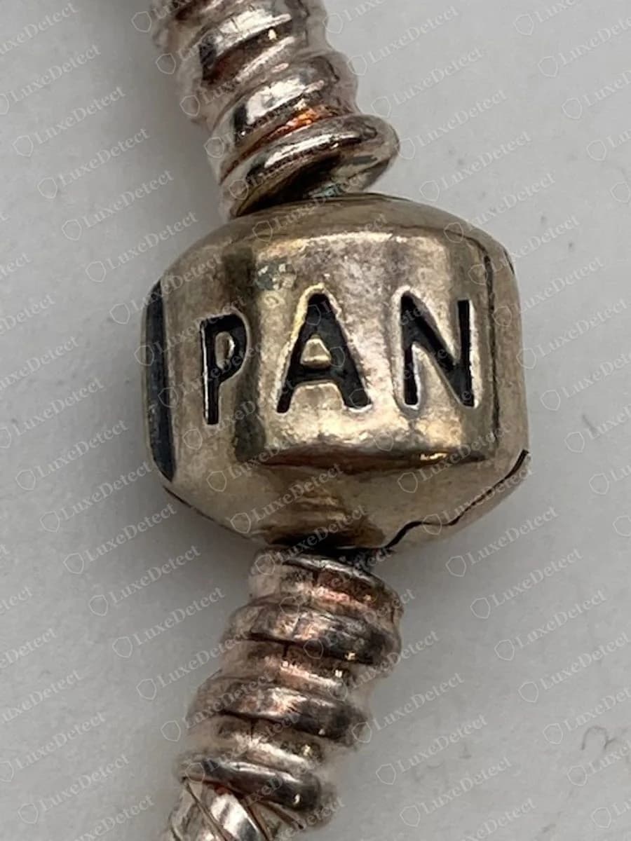 Echter Pandora Tonnenverschluss mit den auf einer Hälfte eingravierten Buchstaben PAN, mit Stoppern mit Gewinde an der Schlangenkette darüber und darunter