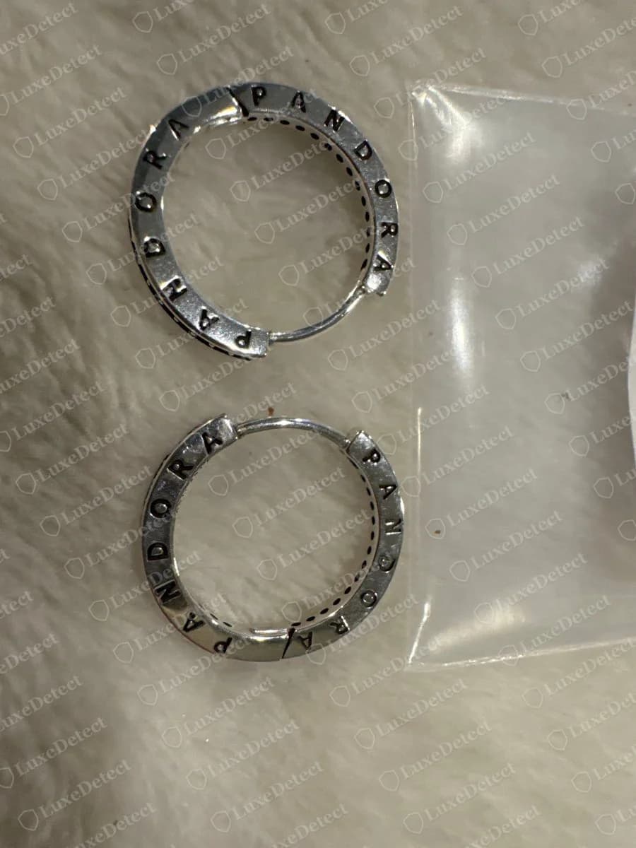 Echte Pandora Silbercreolen mit der Gravur PANDORA rund um jede Creole, neben einem durchsichtigen Plastikbeutel